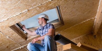 Worker inspecting a skylight installation in a wooden attic.