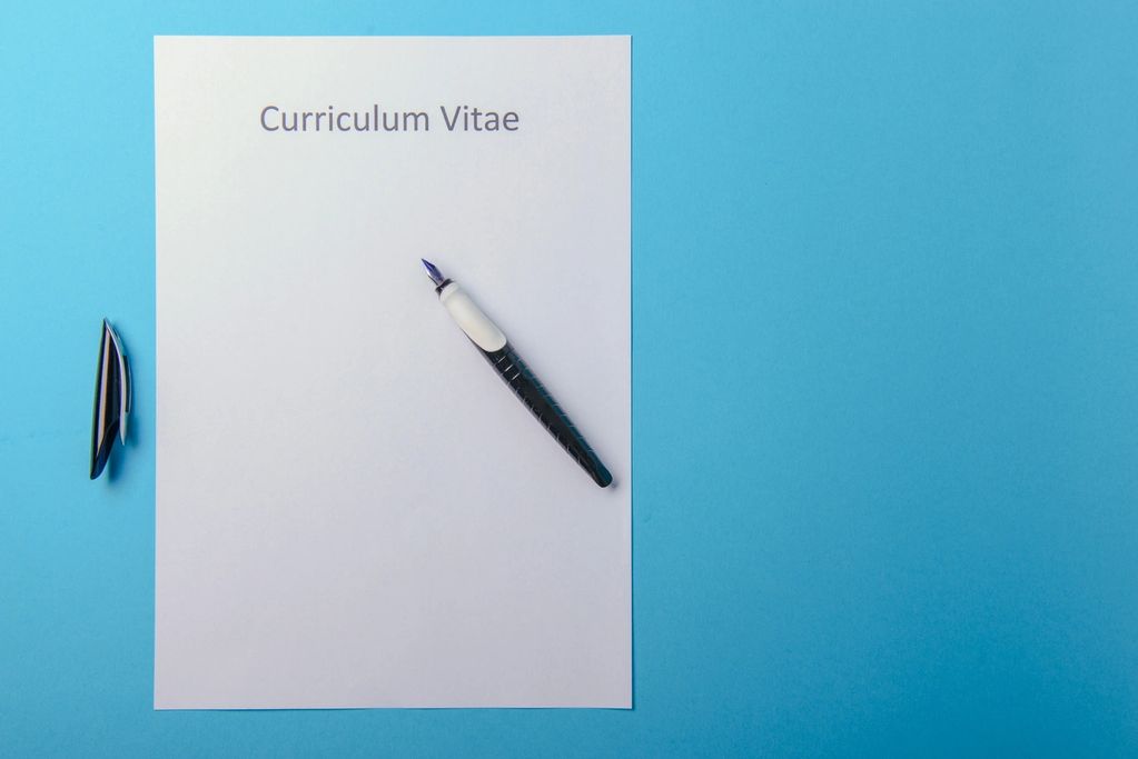 Blank curriculum vitae with pen on blue background.