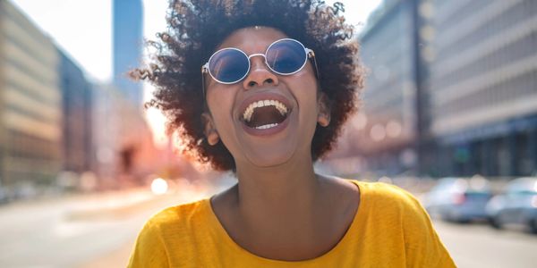 lady with a big smile wearing sunglasses and yellow shirt in a city