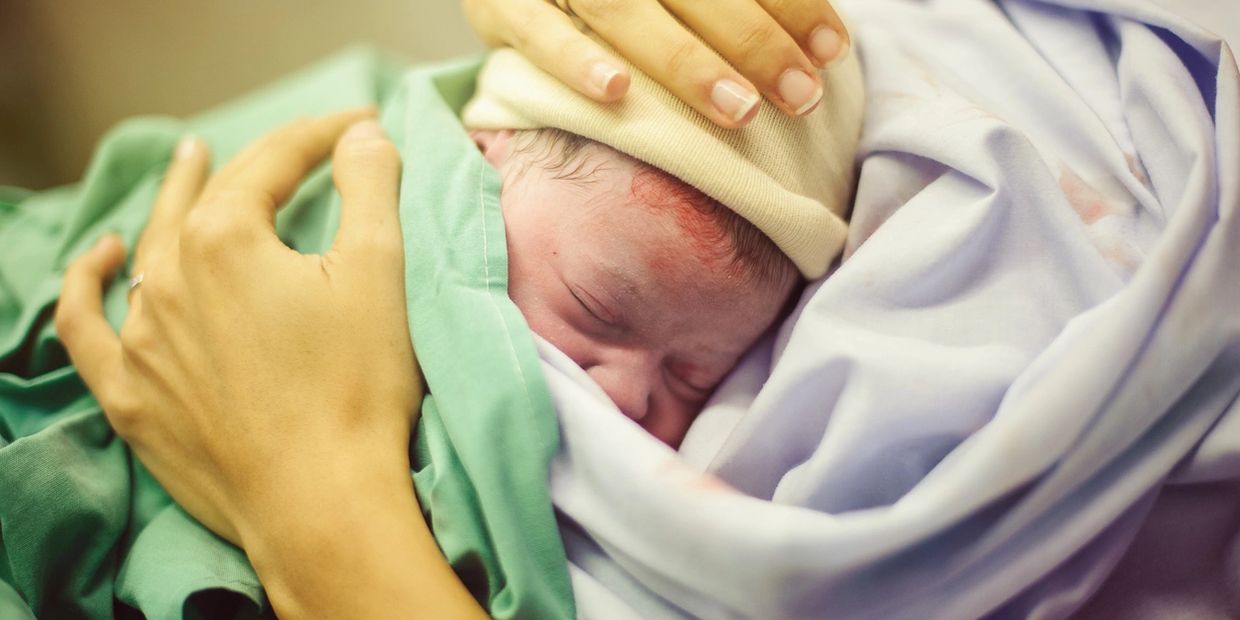 Newborn baby wrapped in blankets being gently held.