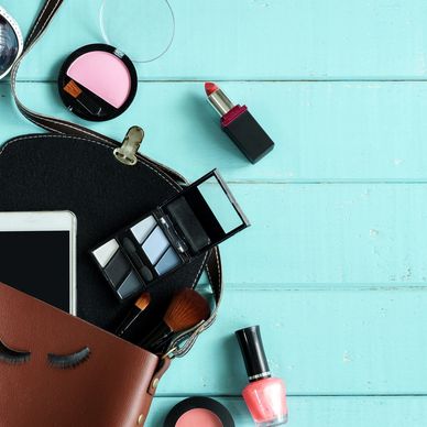 Makeup items and phone spilling out of a purse on a blue wooden surface.