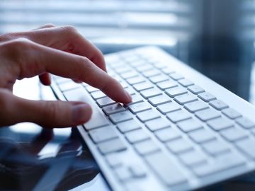 Close-up of a hand typing on a white keyboard.