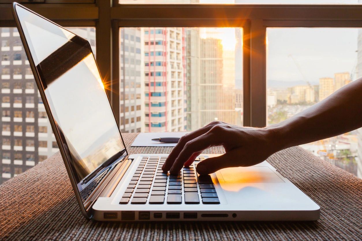 Person typing on a laptop with a city skyline in the background, illustrating the use of digital tools for event marketing and engagement strategies.