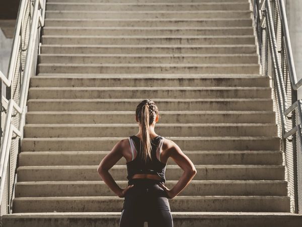 Woman in workout clothes stands at the bottom of a long staircase.