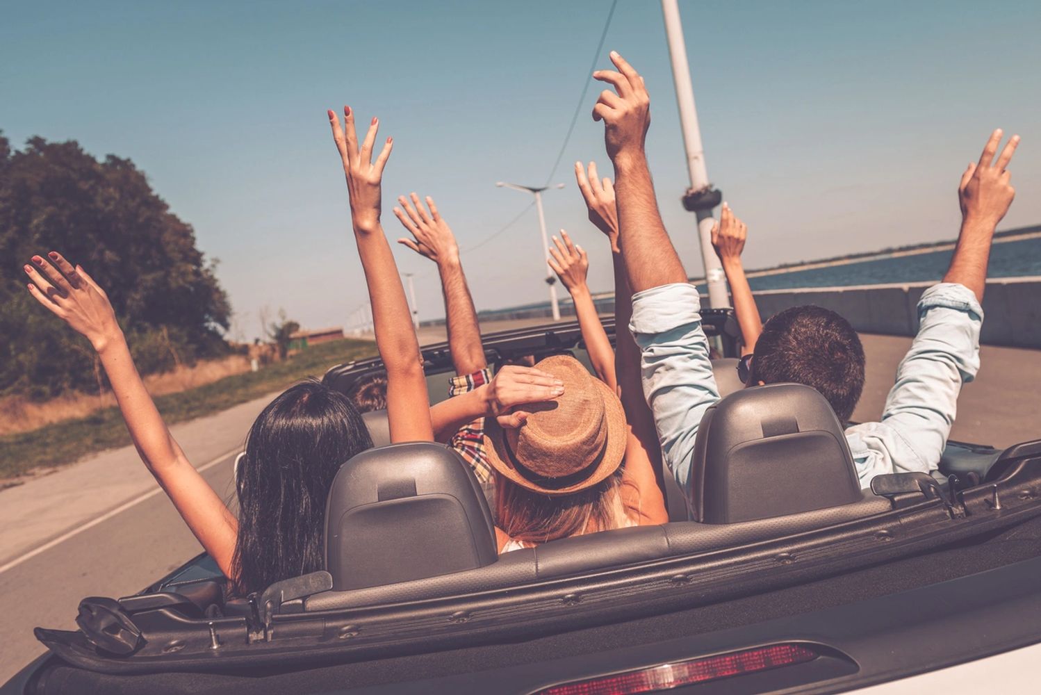 Friends enjoying a convertible road trip with hands raised in excitement.