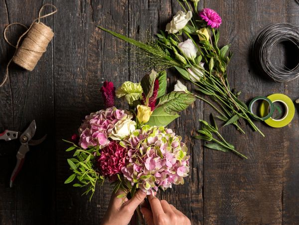 Hands arranging a colorful flower bouquet on a wooden table with floral tools.