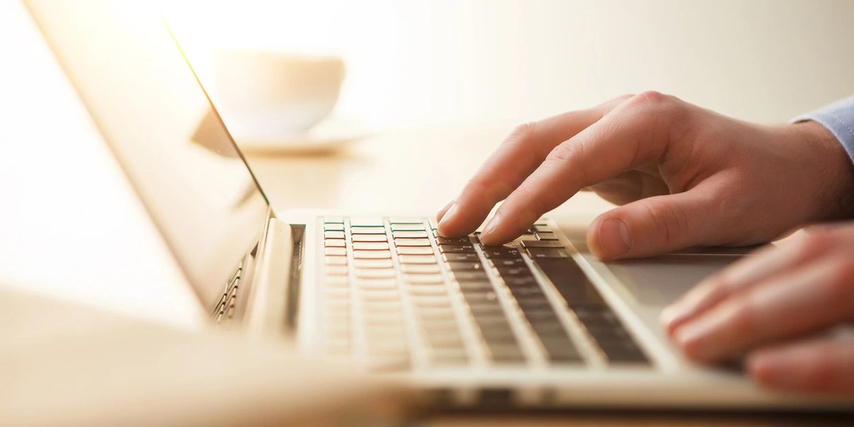 Person typing on a laptop keyboard with warm sunlight.