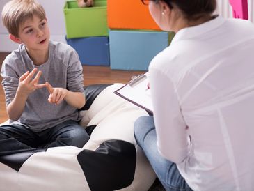 A boy talks to a therapist taking notes during a session.