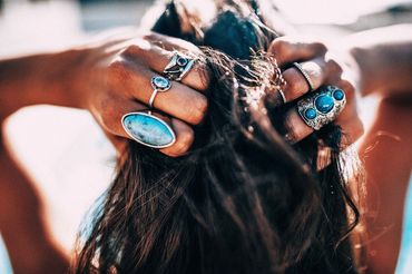 Hands adorned with multiple turquoise rings holding dark hair.