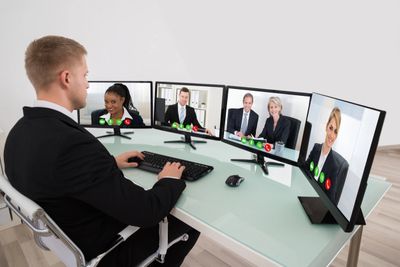 Man in suit video conferencing with four colleagues on multiple monitors.