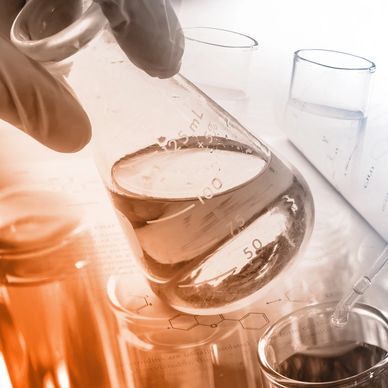 Gloved hand holding a liquid-filled Erlenmeyer flask in a scientific lab setting.