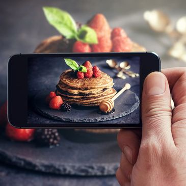 iPhone screen showing image of picture of crepes with fruit with the actual plate seen behind phone