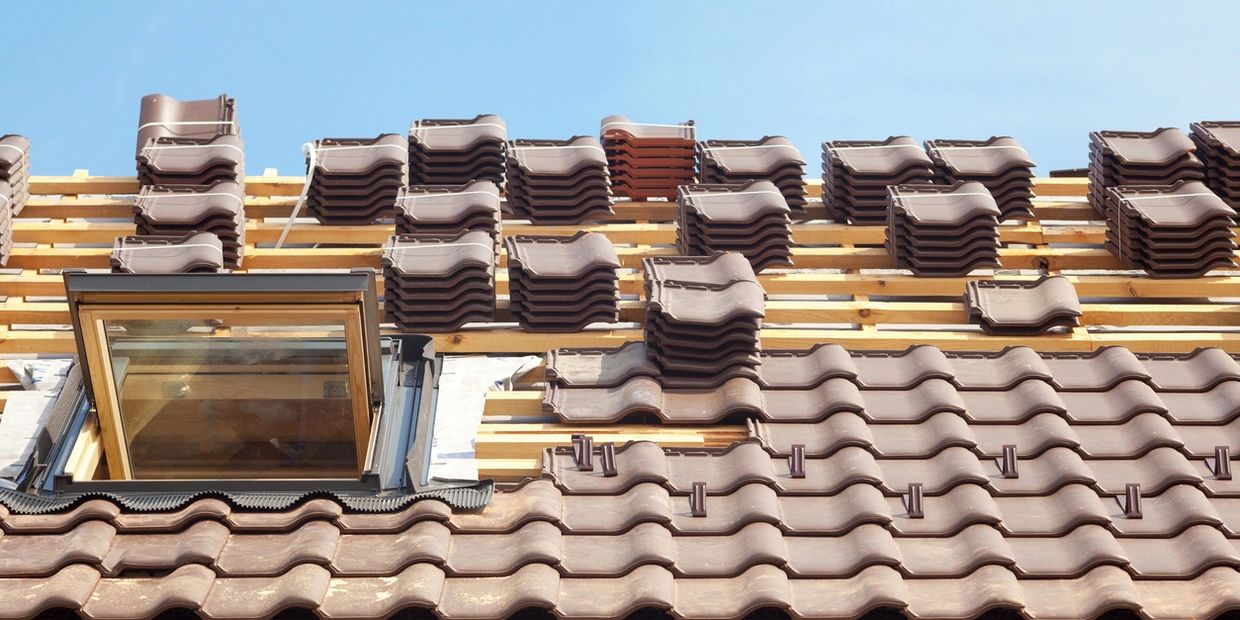 Roofing tiles being installed on a roof with a skylight under a clear sky.