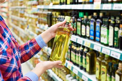 Person holding a bottle of cooking oil in a grocery store aisle.