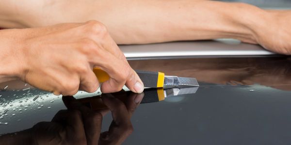 Person removing window tint film with a utility knife on a car window.