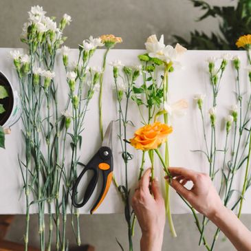 Person arranging white and orange flowers with garden shears on a table.