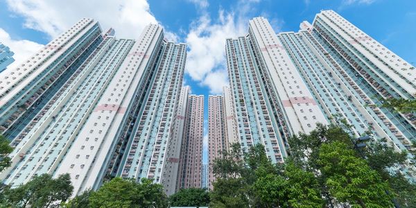 Tall residential skyscrapers under a blue sky with trees in the foreground.
