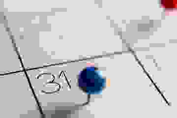 A blue stickpin stuck in a calendar at the 31st date.