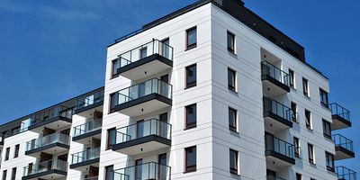 Modern white apartment building with glass balconies under a clear blue sky.