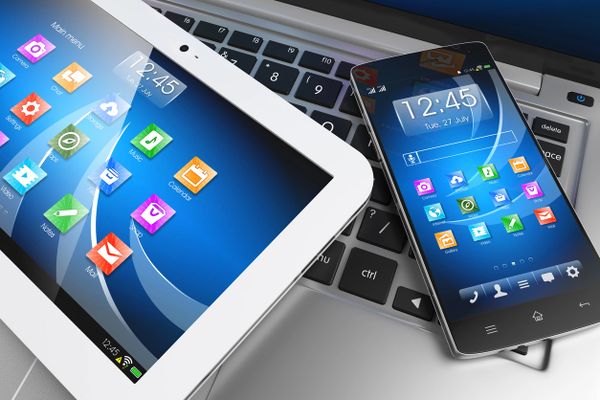 A tablet and smartphone resting on a laptop keyboard, both displaying colorful app icons.