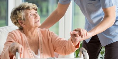 Elderly lady in sitting position being helped to use walker by aide