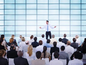 Businessman presenting to a large audience in a modern conference room.