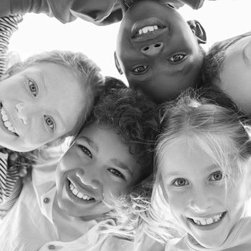 A group of diverse children smiling in a circle, looking down at the camera.