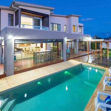 Modern house with a lit swimming pool and outdoor seating at dusk.