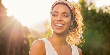 Smiling woman enjoying sunlight outdoors with a colorful headband.