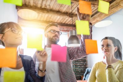 Three diverse people strategizing with sticky notes on a glass wall