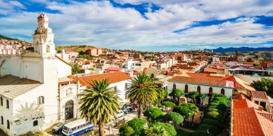 Sunny cityscape with historic buildings and palm trees under a bright blue sky.