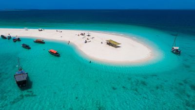 White sand island in turquoise waters with boats anchored nearby in Zanzibar, Tanzania.