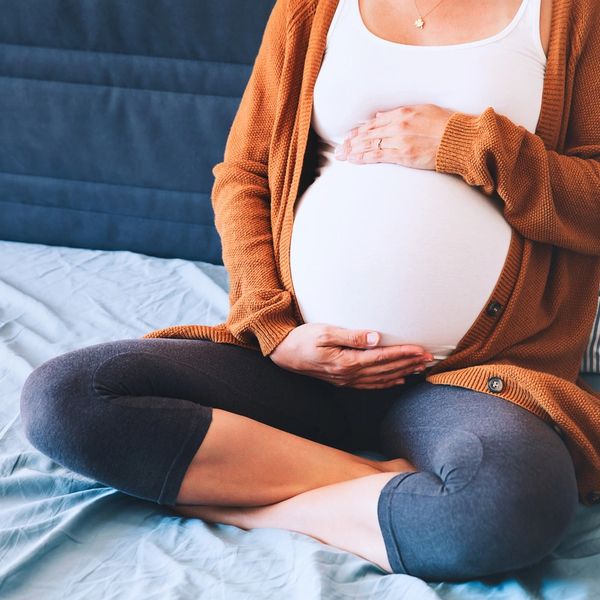 Seated, pregnant woman, with hands at the top and bottom of her round stomach.