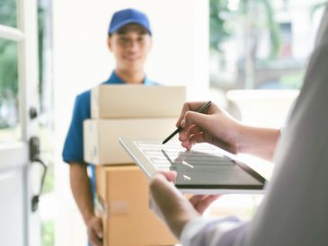 A delivery person holding packages while a customer signs on a tablet.