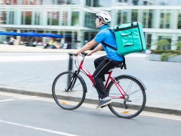 Delivery person riding a bicycle with a large insulated backpack.
