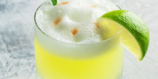 Yellow cocktail with foam and lime wedge garnish.