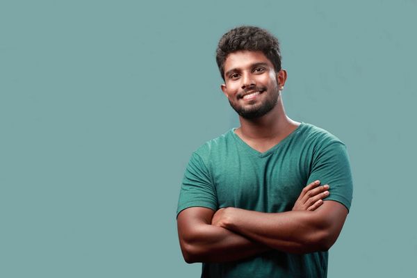 Smiling man with crossed arms wearing a green shirt against a blue background.