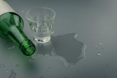Green bottle spilled water next to a glass on a gray surface.