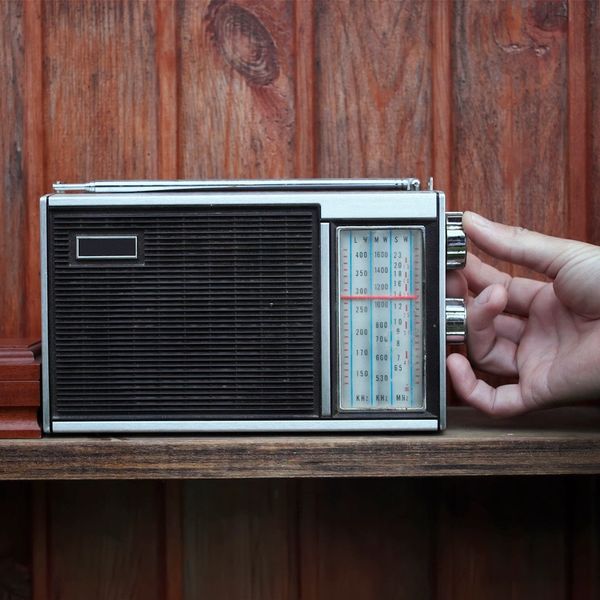 Hand tuning a vintage radio on a wooden shelf.