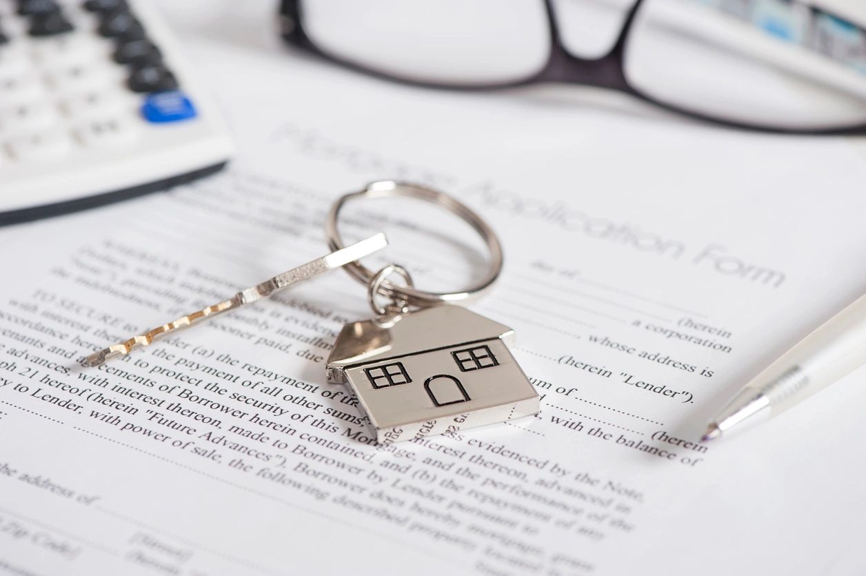 An agreement of sale sits beneath the new keys to a home on top of a table with a calculator, glasses and pen also on the table.