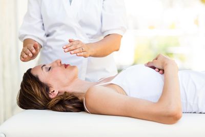 A lady lying on the table while hand are hovering over her face for a reiki treatment.