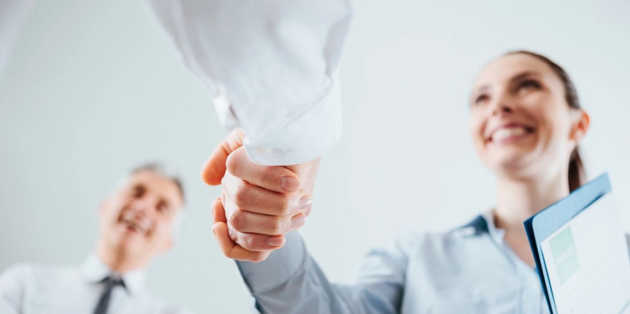 Two professionals shaking hands, smiling and closing a deal.
