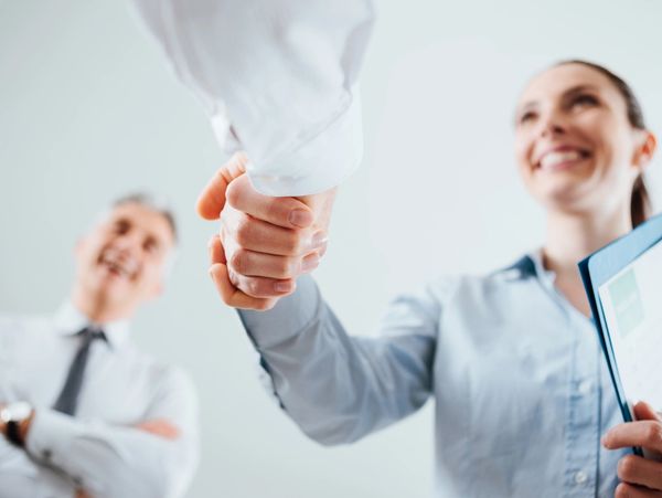 Two professionals shaking hands with a third smiling in the background.