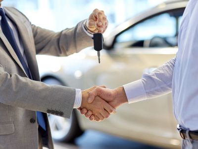 Two people shaking hands as one holds car keys, indicating a car sale or agreement.