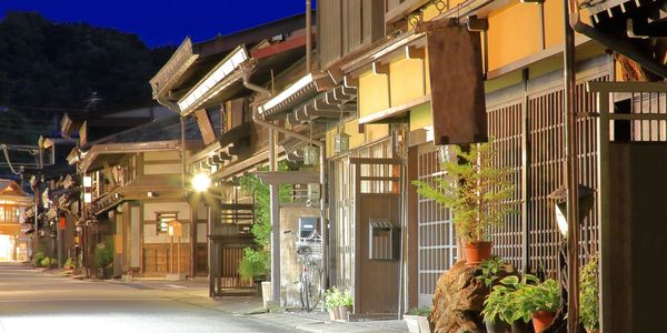 Quiet street with traditional wooden buildings lit warmly at night.