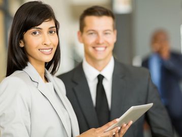 Two professionals smiling, one holding a tablet.