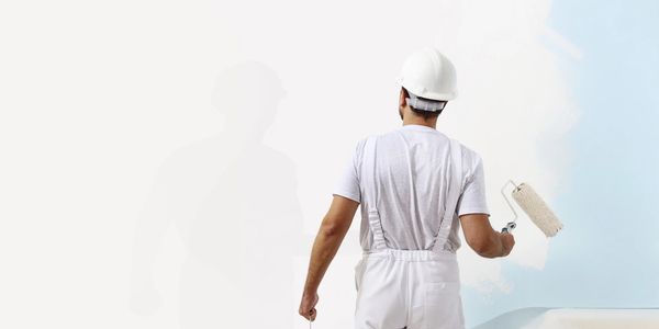 Painter in white overalls and helmet painting a wall light blue.