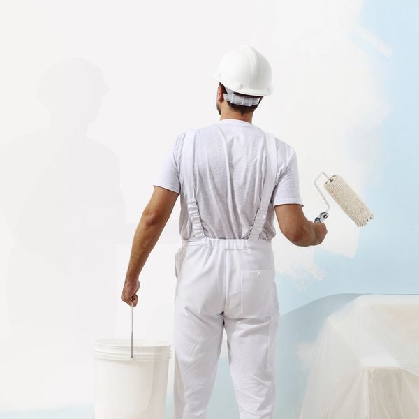 Painter in white overalls and helmet painting a wall light blue.