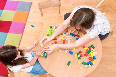 Two children playing with colorful building blocks at a wooden table.