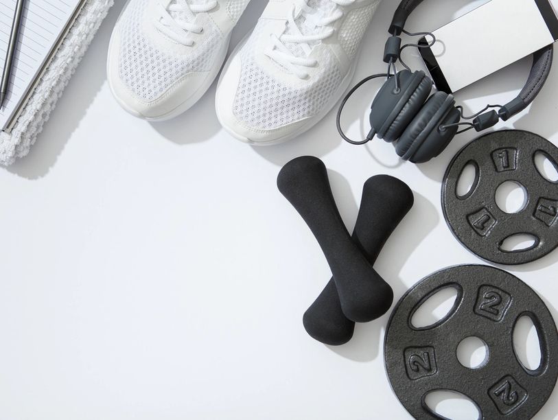White sneakers, dumbbells, weight plates, and headphones on a white surface.